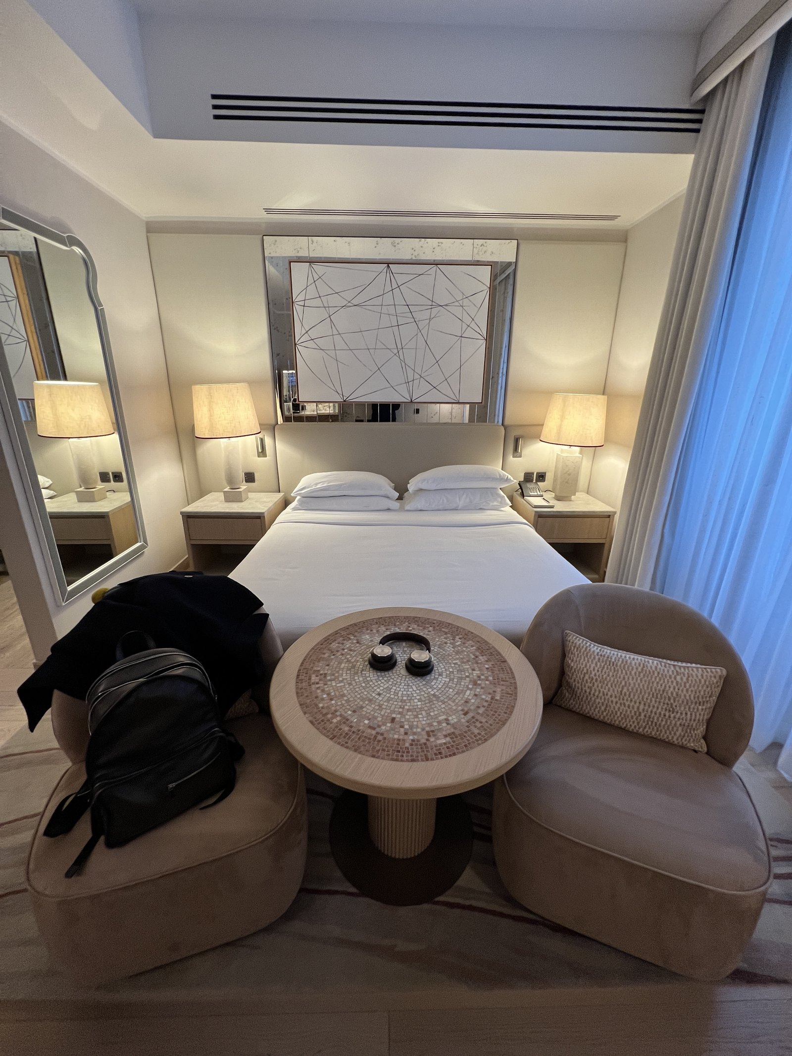 A king bed with white linen in a room with a large abstract picture above it