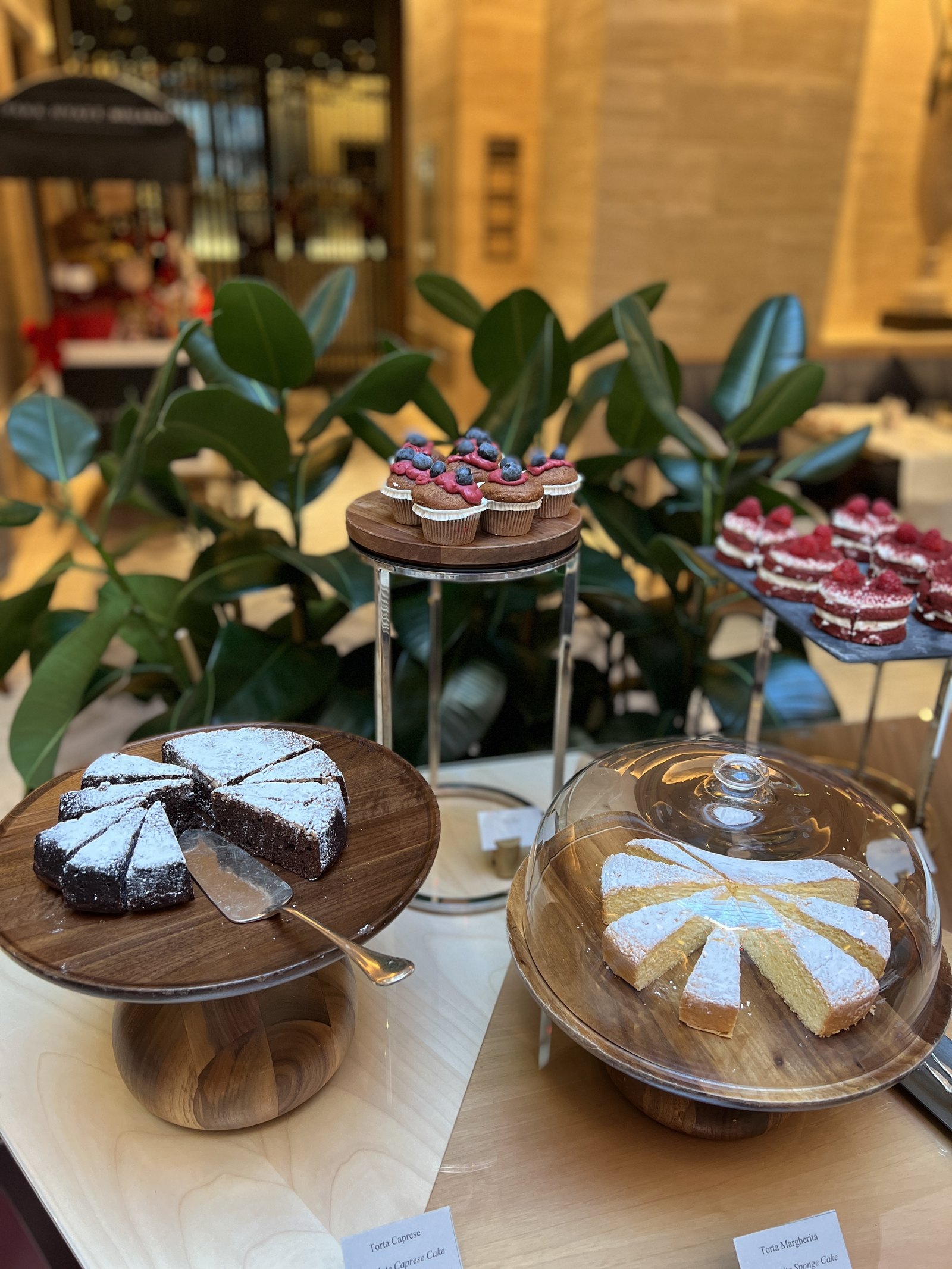 Chocolate and white cakes on a glass stand, beside small pastries under a glass cover