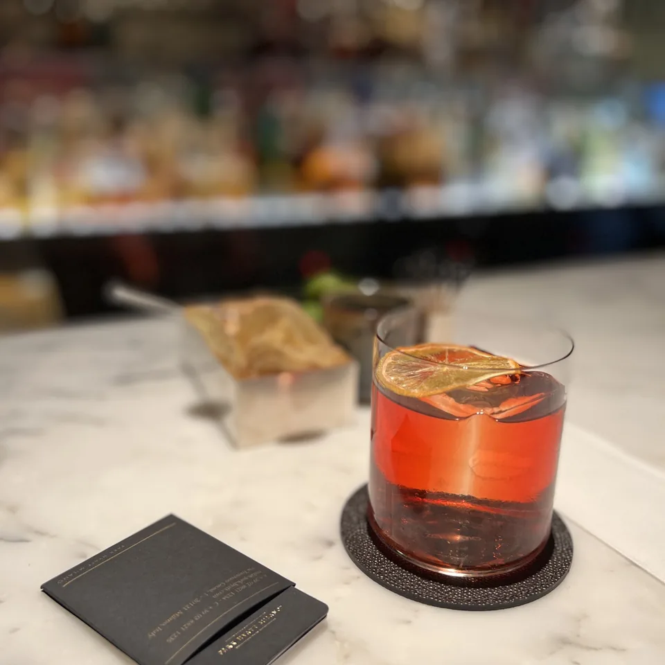 An orange-twisted cocktail in a rocks glass on a marble counter, with the hotel's card beside it