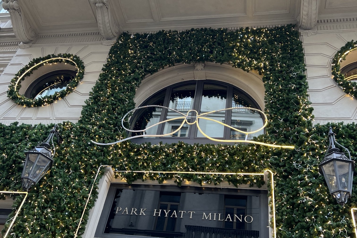 The entrance of Park Hyatt Milano under a canopy of garland and white lights, with a large white bow over the arch and the hotel's name above the door