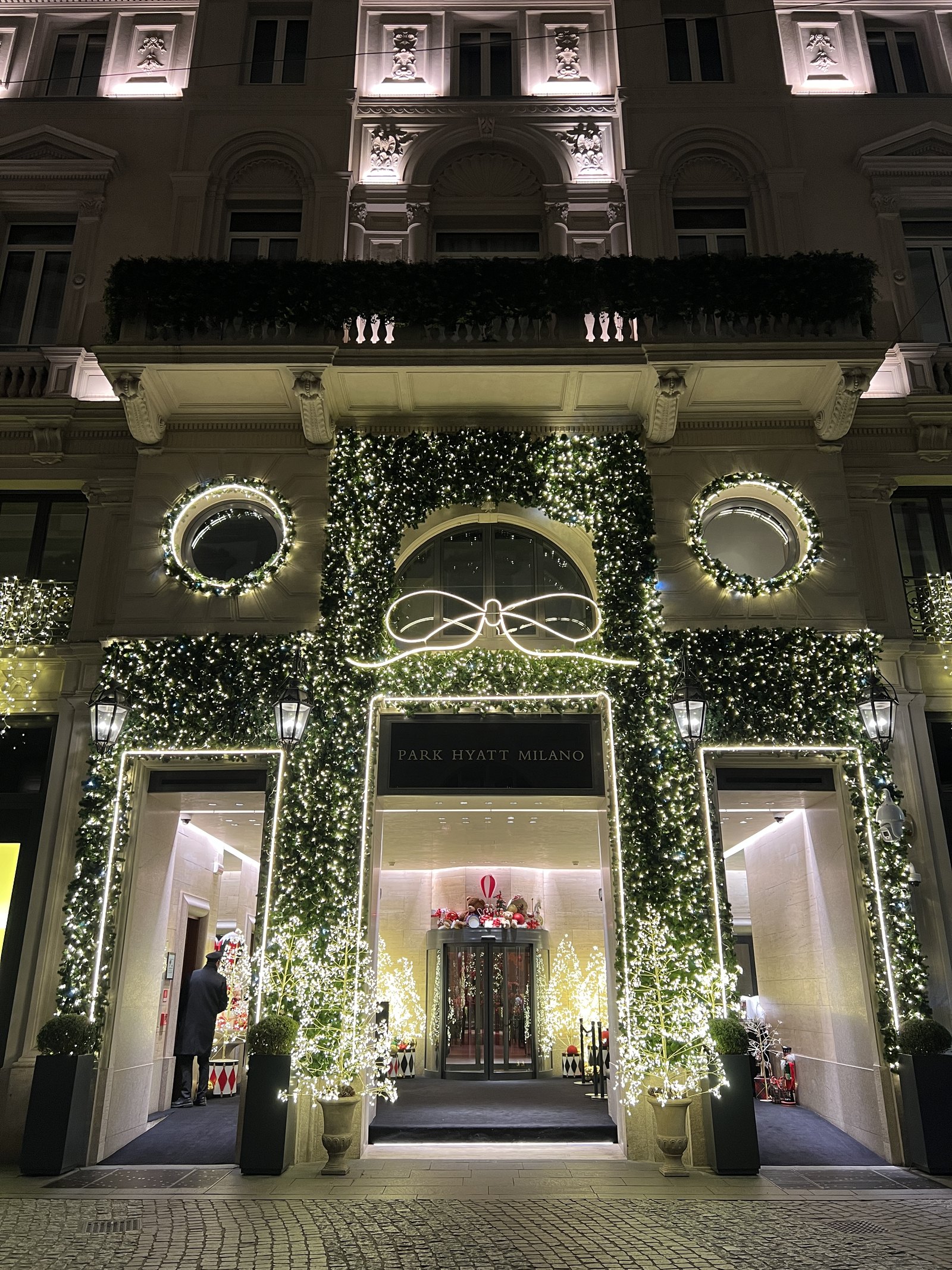 The arched entrance of Park Hyatt Milano at night, wrapped in white lights and a large bow