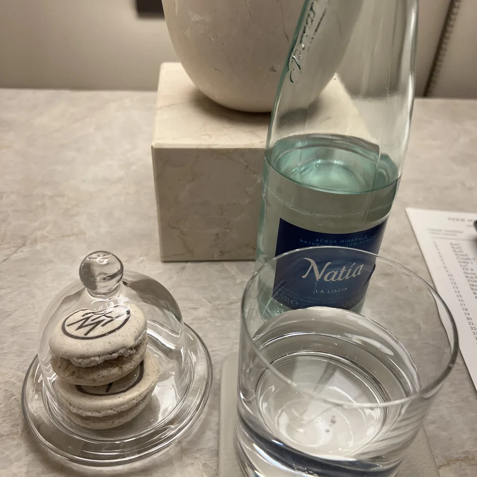 Two macarons under a glass cloche beside a bottle of water and a glass