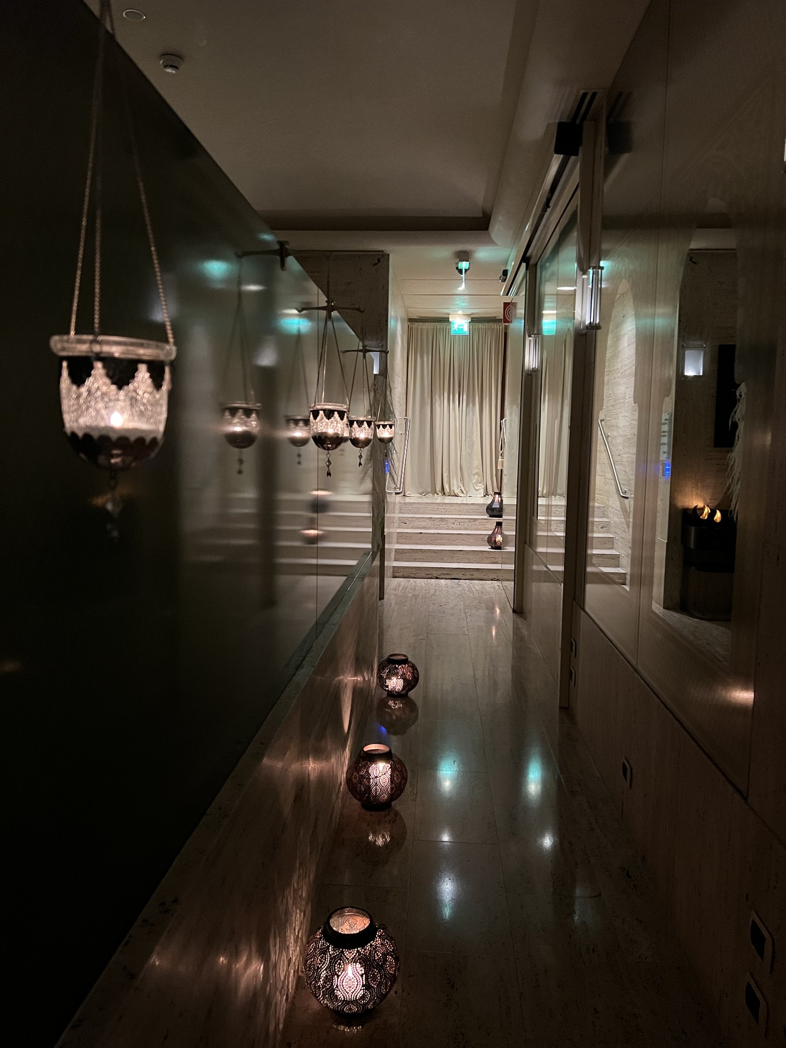 A dark corridor with glass lanterns hanging on the wall and light reflected in the floor