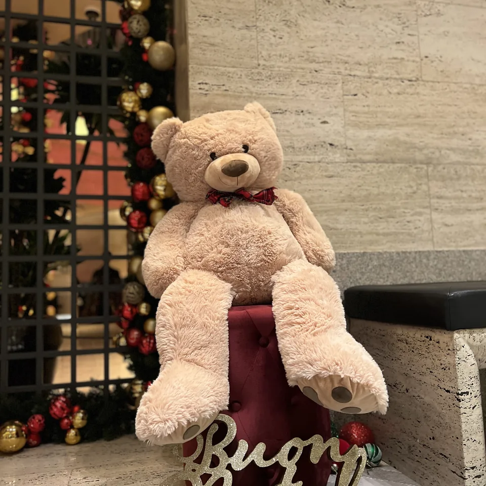 A large cream teddy bear seated on a red cushion beside a gold sign that reads Buon Natale
