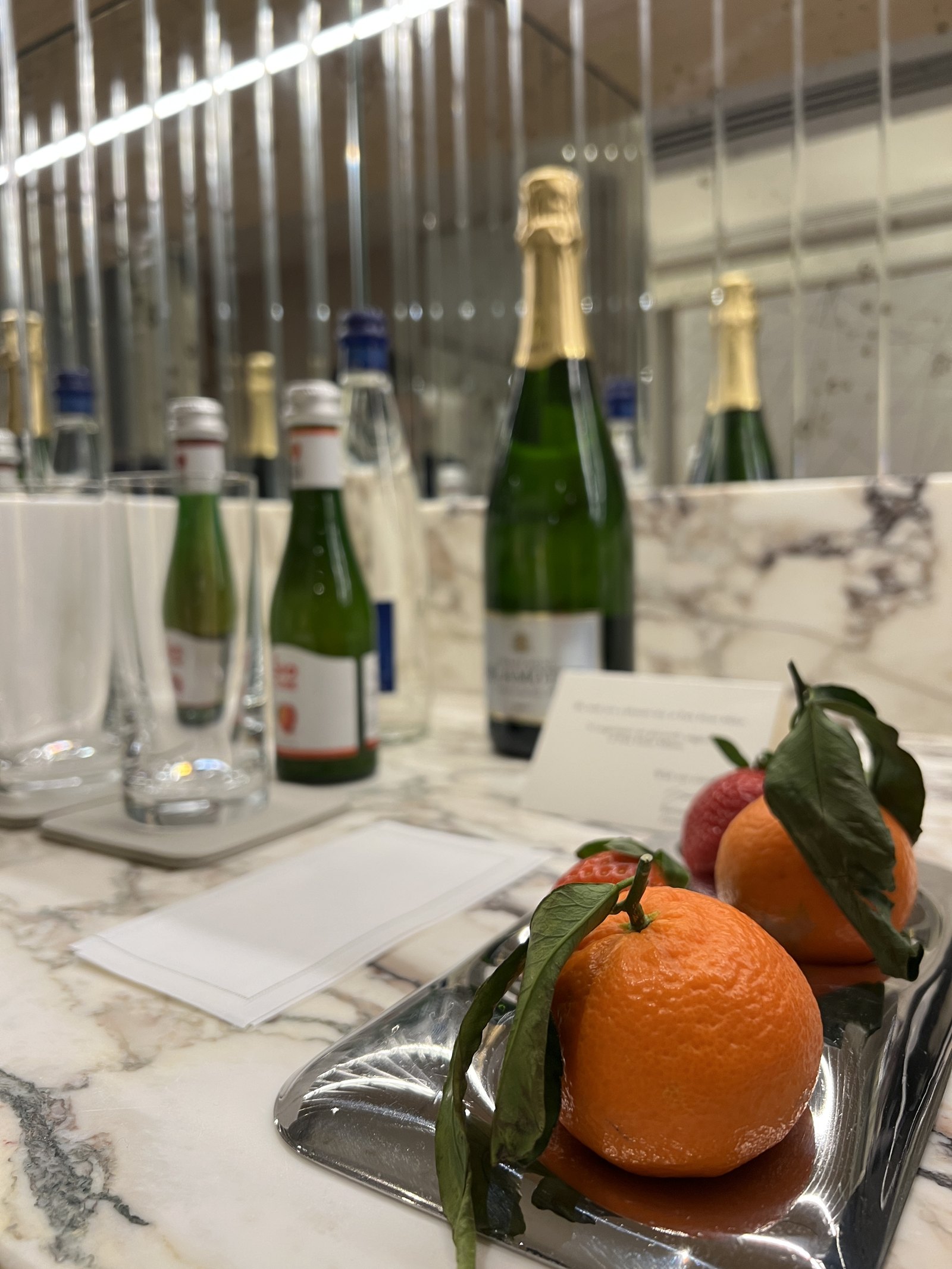 Champagne bottles and glasses on a white-clothed table, with clementines on a silver tray