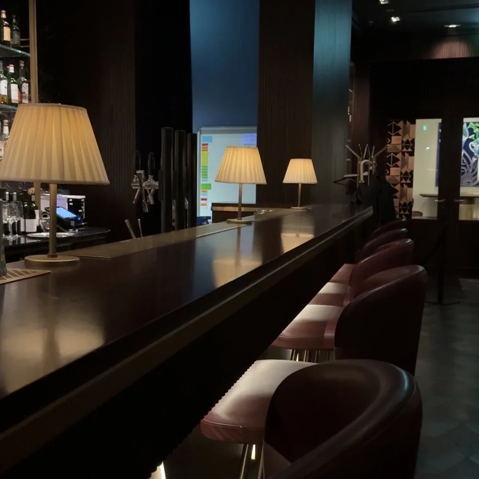 A long bar counter at night with lamps down its length and stools in a row