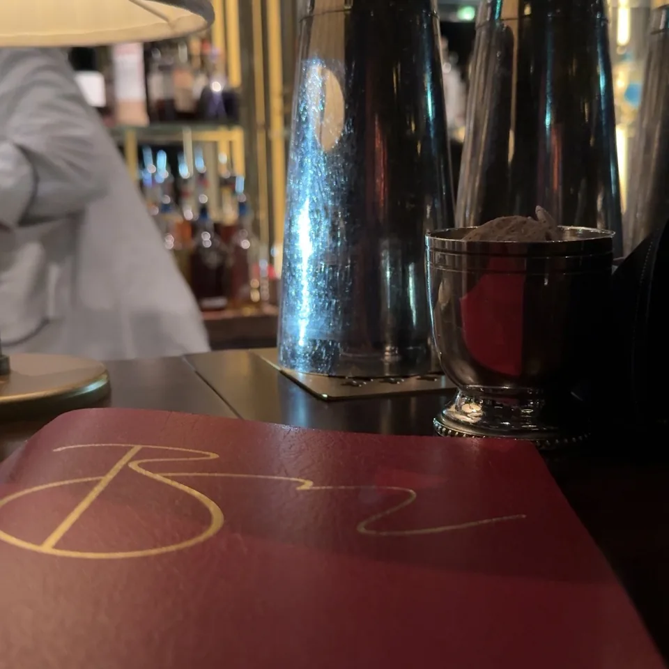 A shaker and a filled glass on a red leather counter under a pleated lampshade