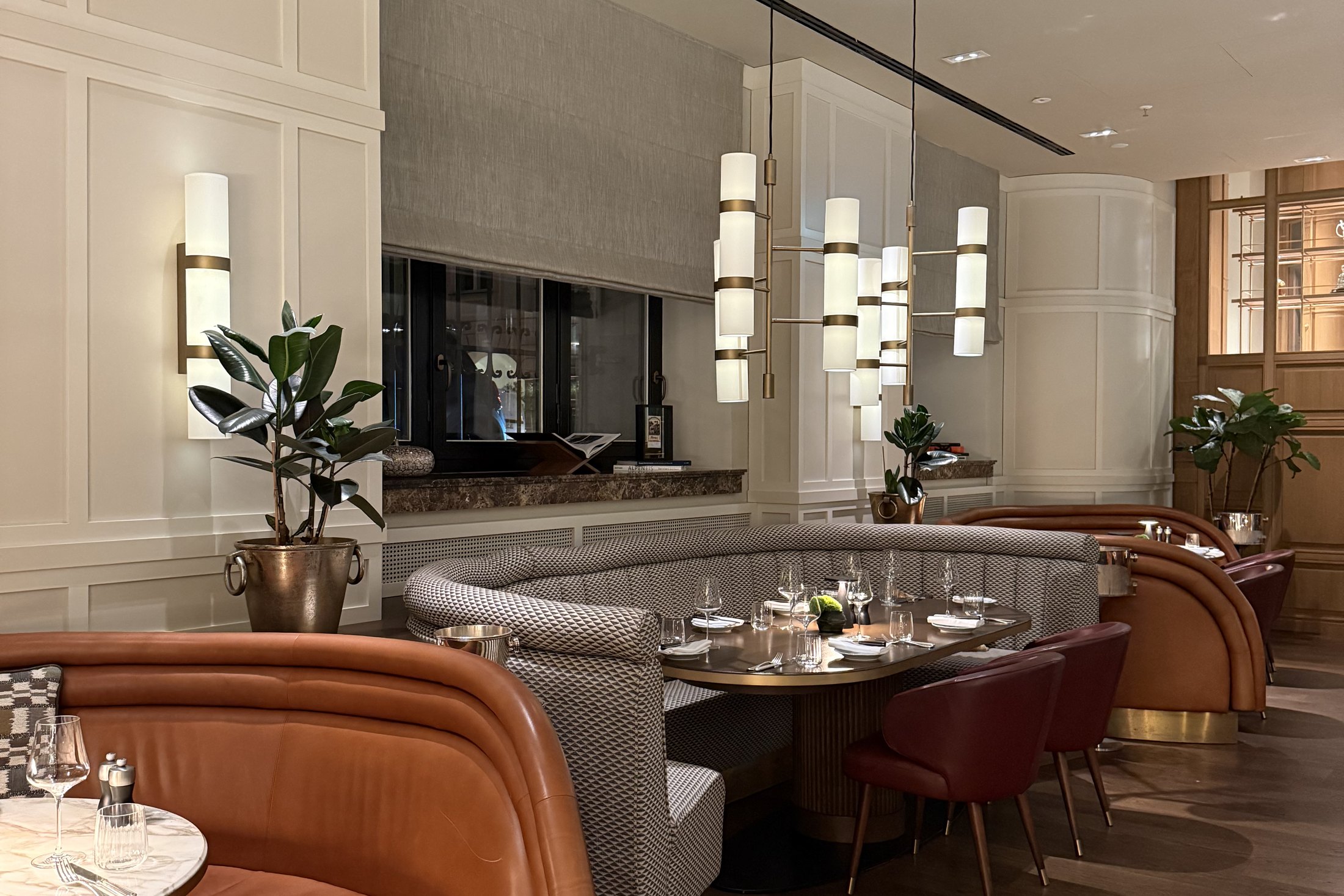 A brasserie room with orange and red banquettes, panelled walls and low pendant lamps