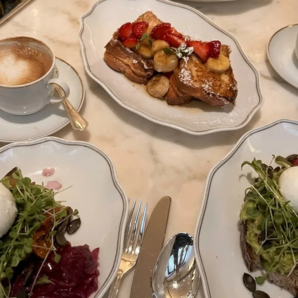 Breakfast on marble: French toast with strawberries, a fruit plate, avocado toast and a cappuccino