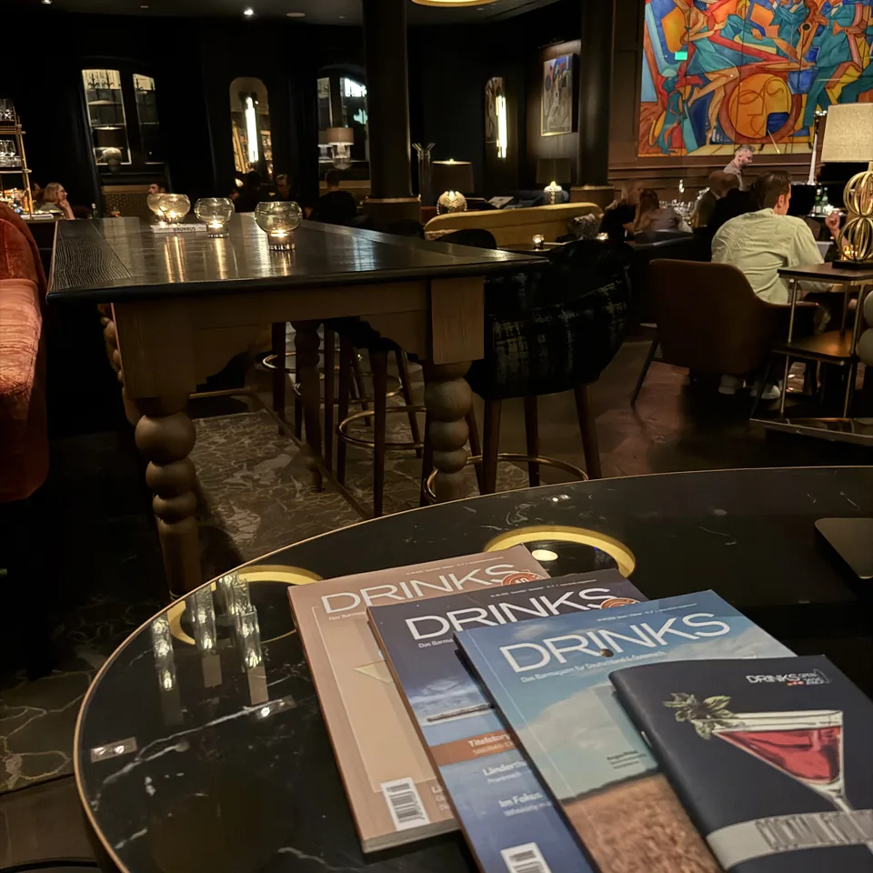 Three drinks menus fanned on a round black table in front of a lit bar