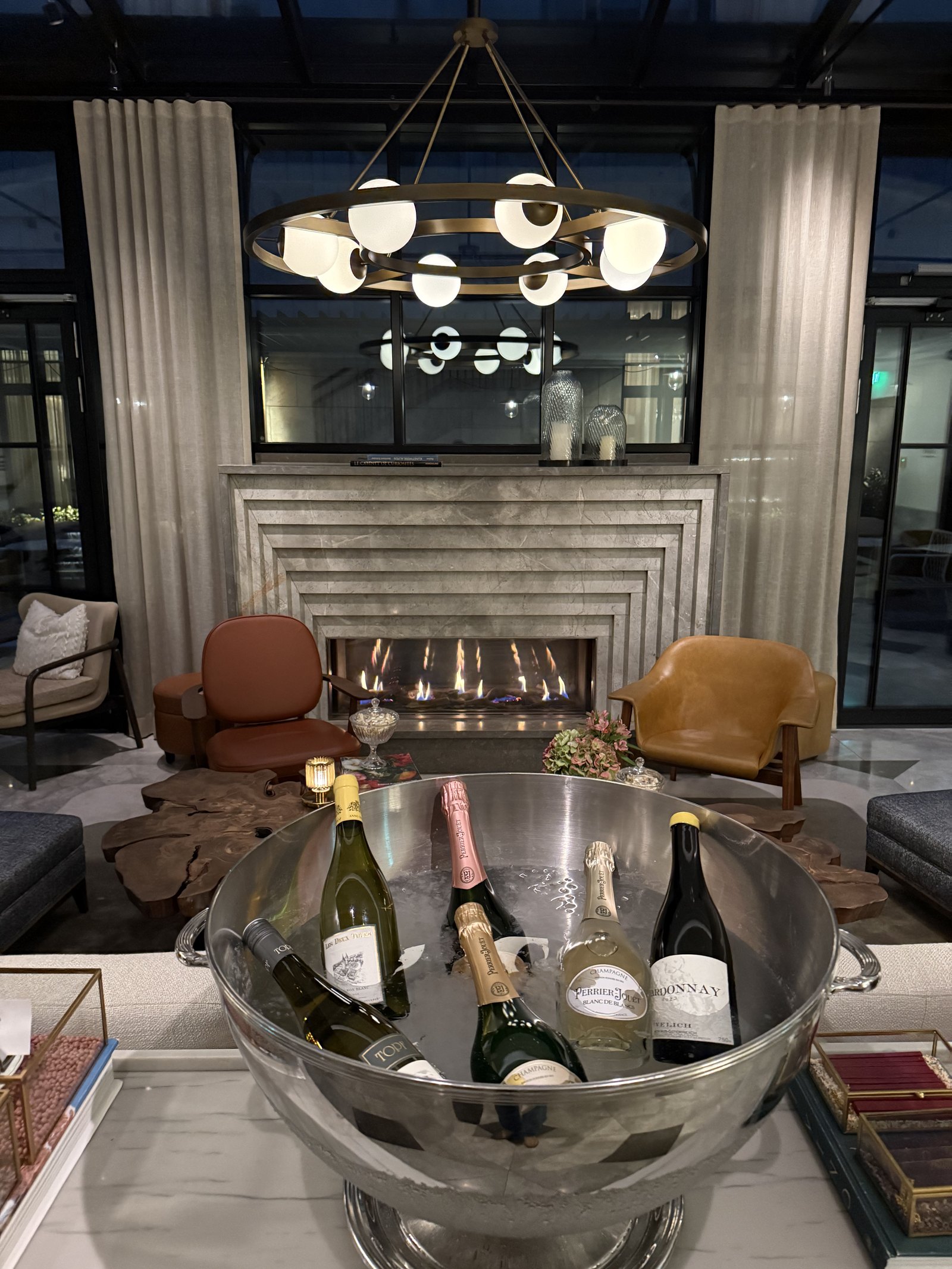 A silver bowl of champagne bottles on ice in front of a stone fireplace with leather chairs around it