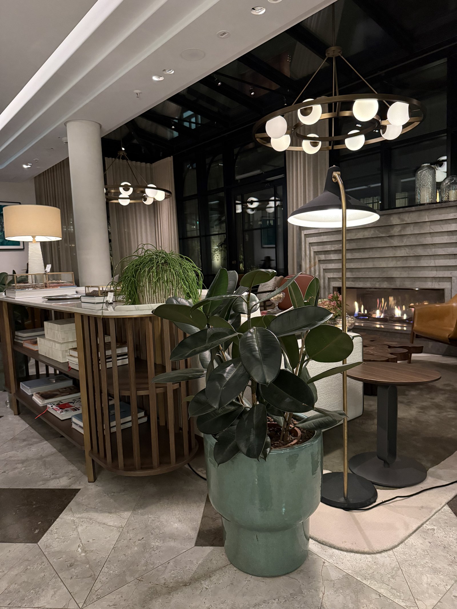 A lobby with marble floors, a tall plant in a green pot, lamps and a bar counter beyond