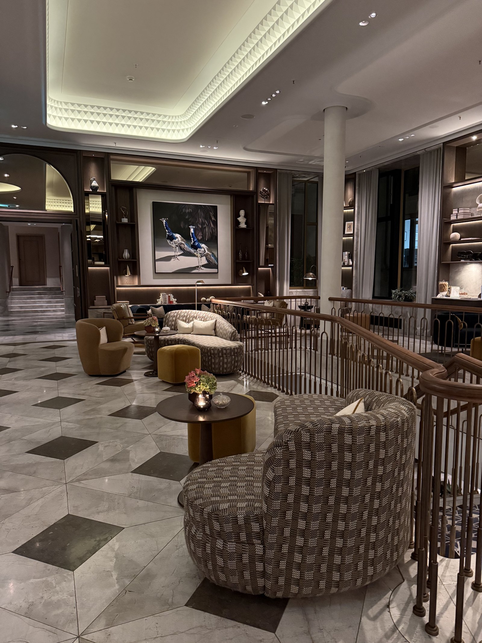 A lounge seen from a landing, checkerboard marble floor, armchairs and bookshelves under a chandelier
