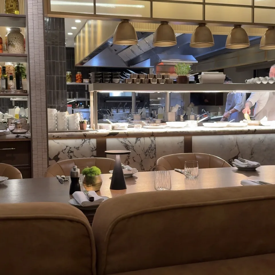 An open kitchen behind glass with brass pendant lamps over tan banquettes