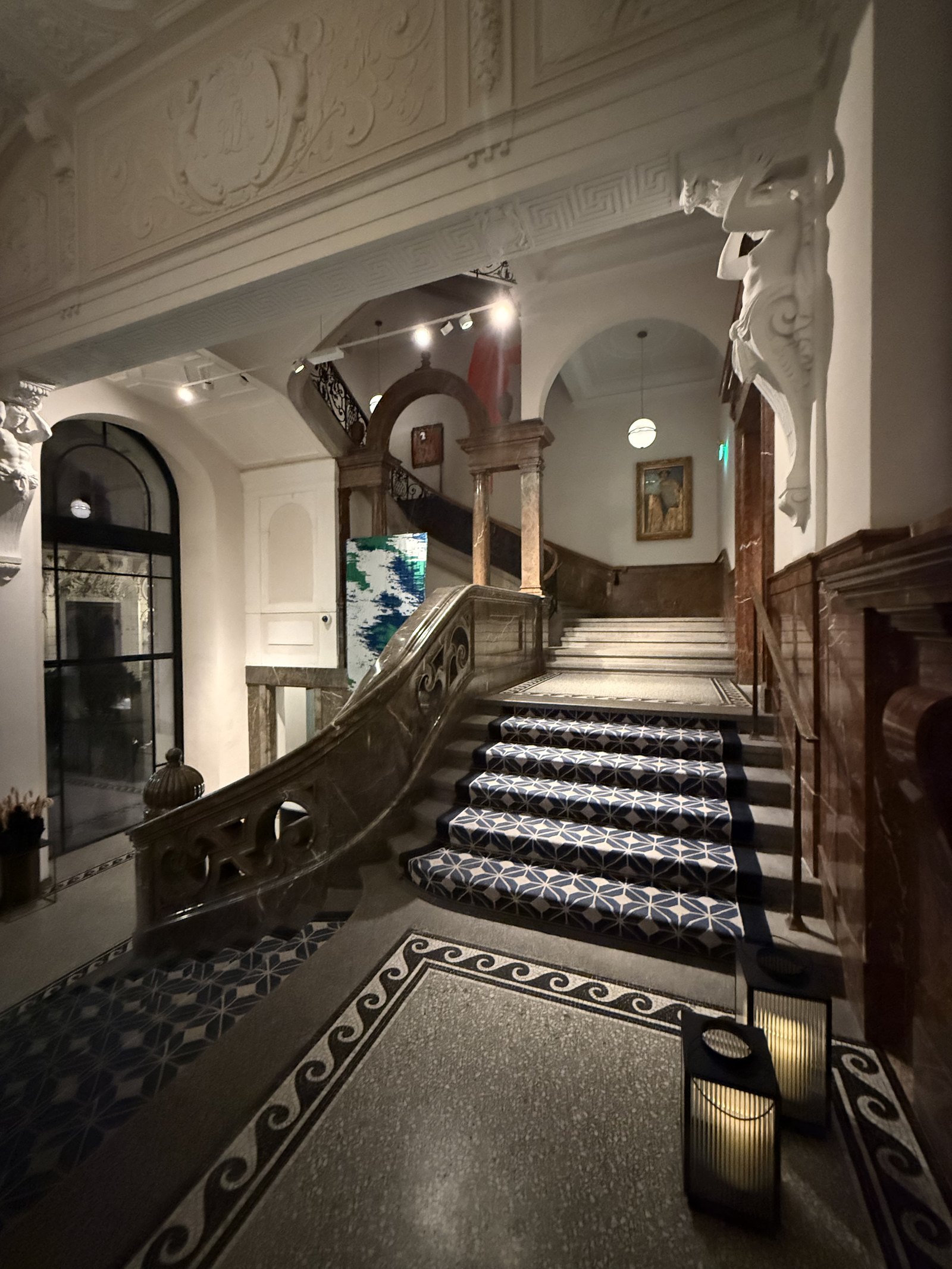 A marble staircase with a patterned blue and white runner, carved stone figures above and lanterns on the terrazzo floor