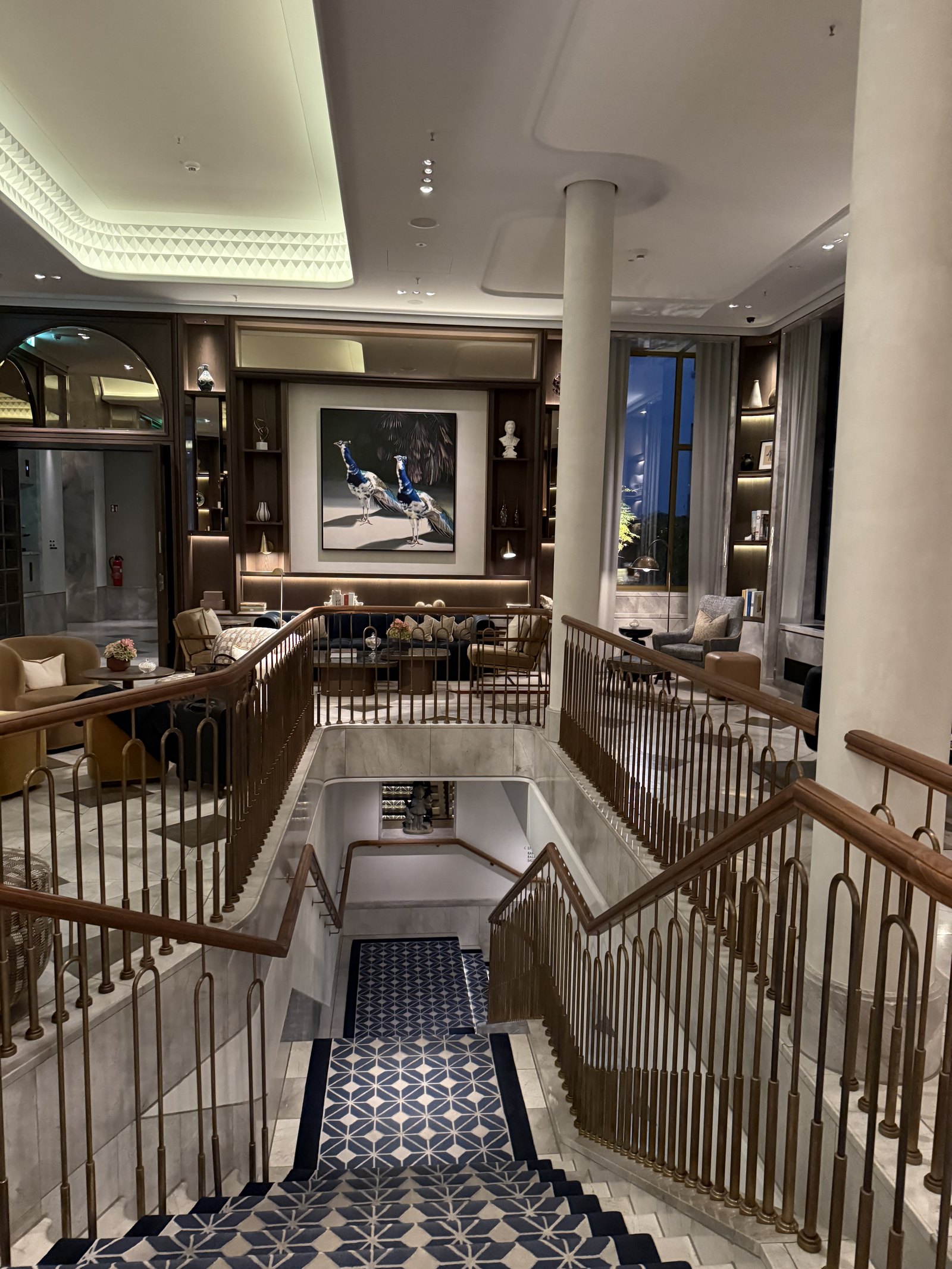 A staircase seen from the landing above, its runner running down between brass balusters