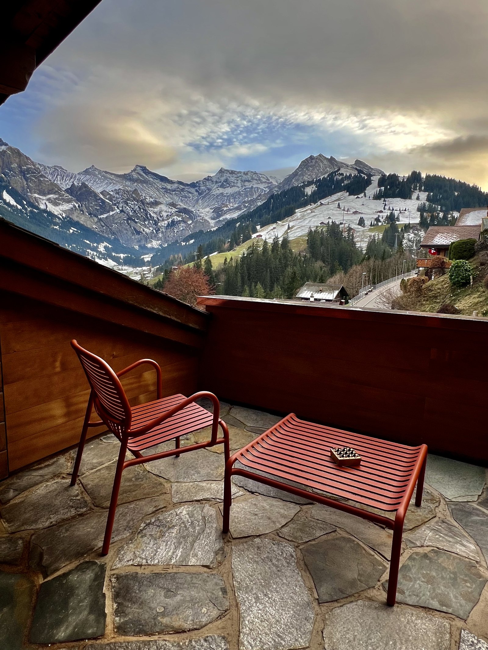 A balcony at The Brecon with red metal chairs and a bench on stone flags, the valley and the first snow on the peaks beyond