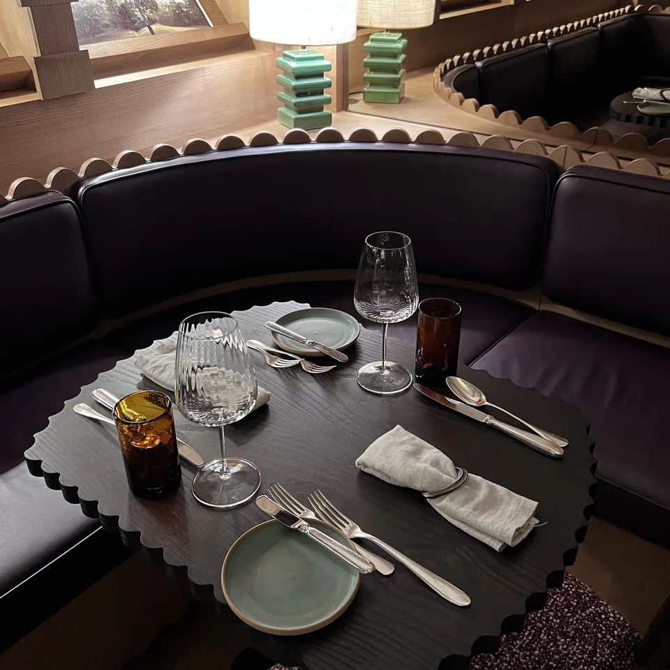 A scalloped edged table laid for dinner in a leather banquette corner under two shaded lamps