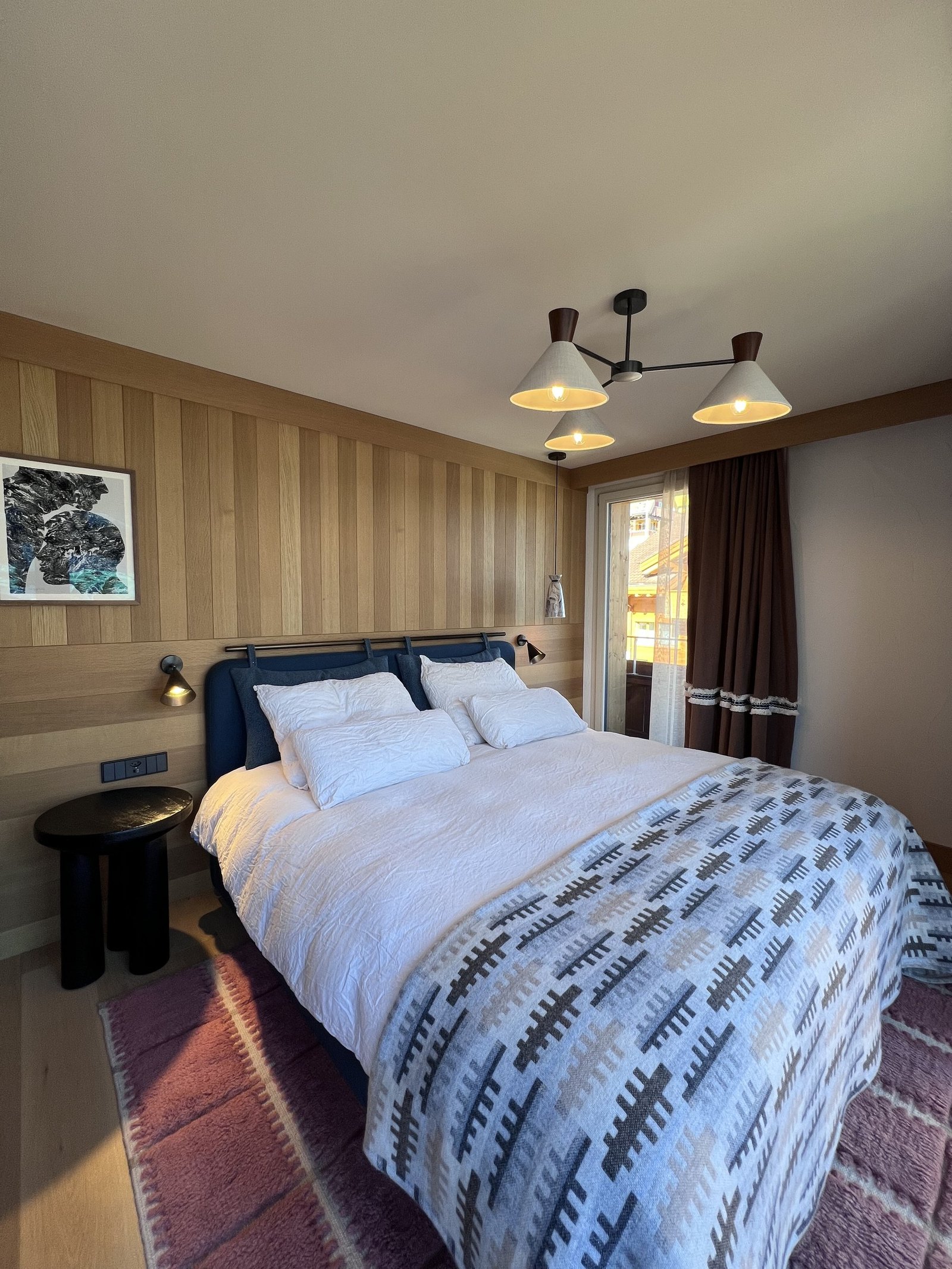 A bed with a black headboard and a patterned alpine blanket, on a striped runner rug
