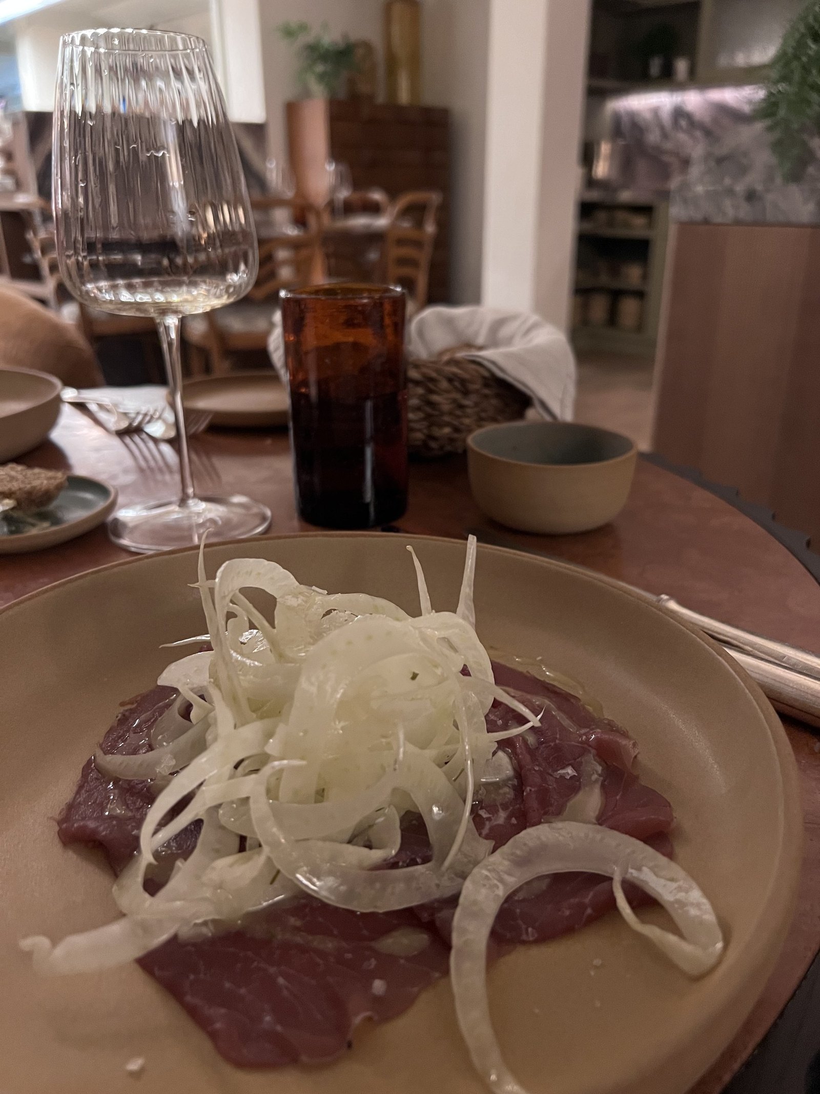 A plate of beef carpaccio with shaved fennel and a glass of red wine beside it