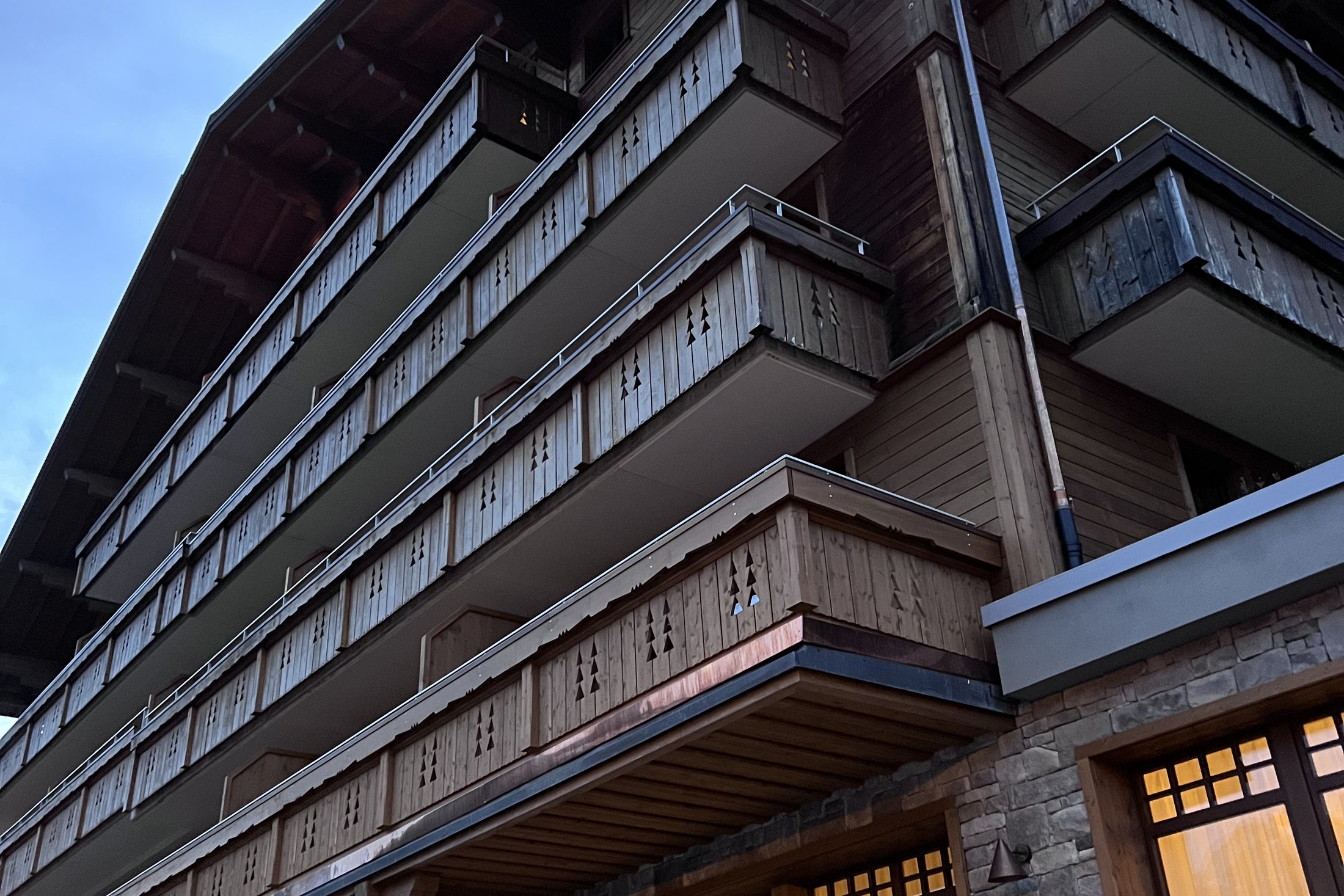The timber facade of The Brecon from below, with four storeys of carved balconies and lit windows at the base