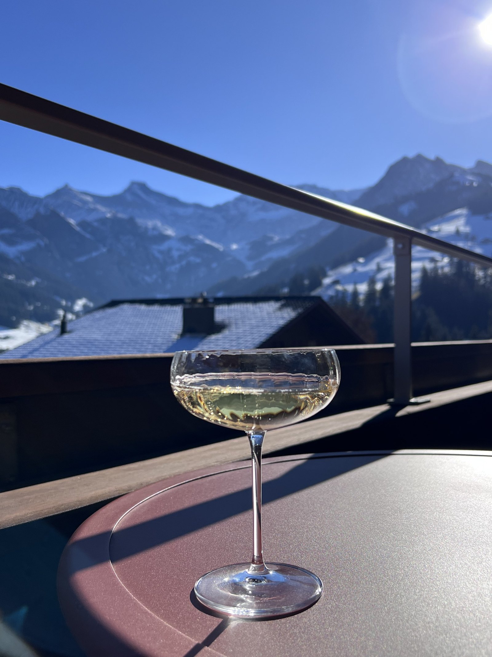 A coupe glass standing on the balcony rail with the snow covered mountains beyond