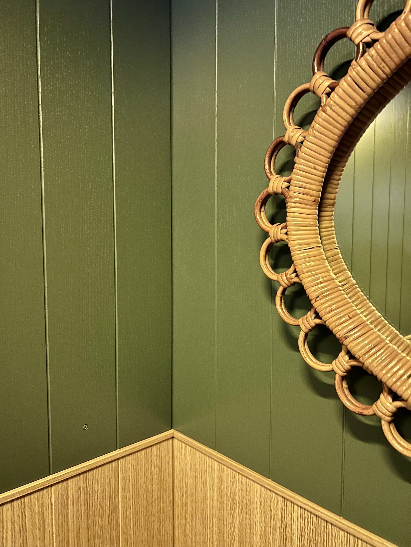 A corner panelled in olive green with a scalloped rattan mirror
