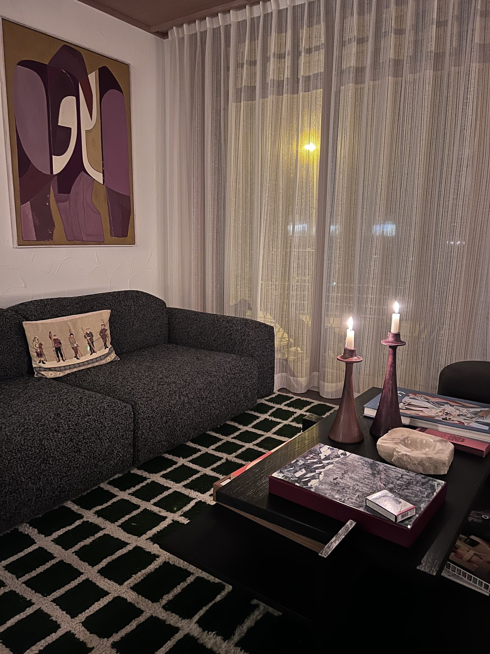 A sofa with lit candles on a low table, art on the wall and a checked rug