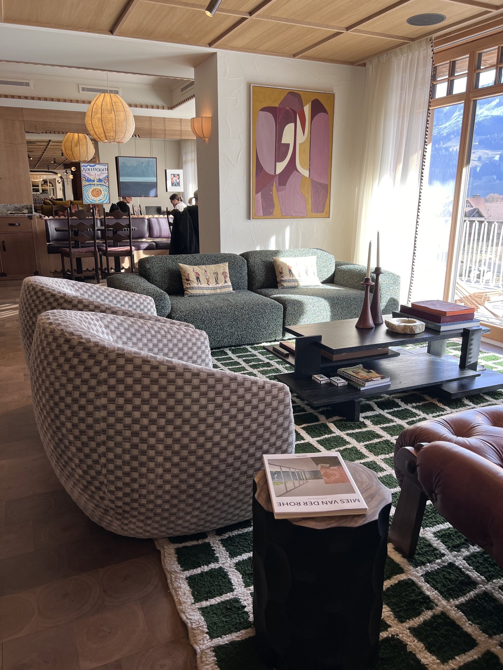 A lounge at The Brecon with armchairs on a green checked rug, paper lanterns overhead and windows onto the mountains
