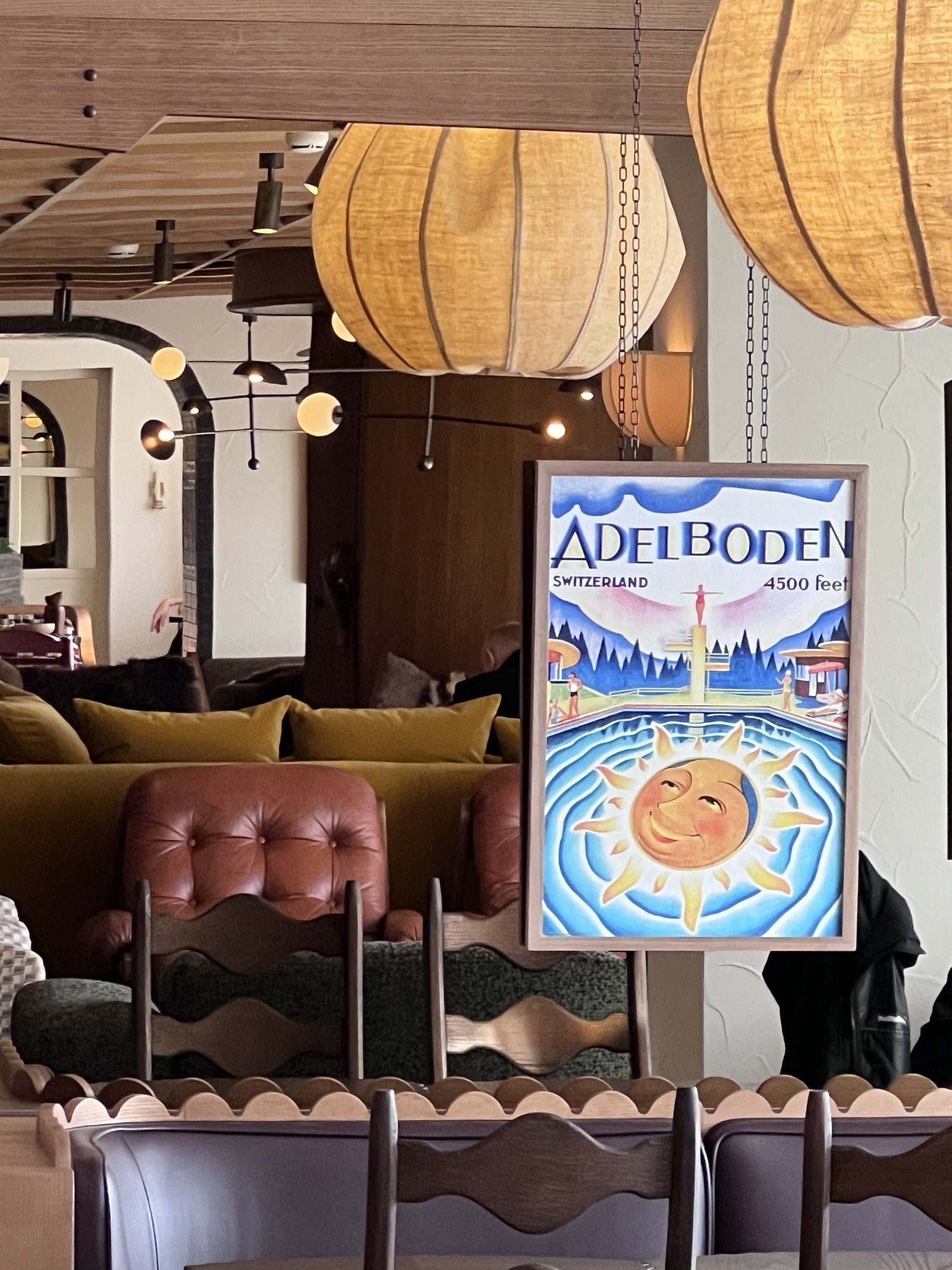 A lounge with leather banquettes, paper lanterns and a framed vintage Adelboden travel poster