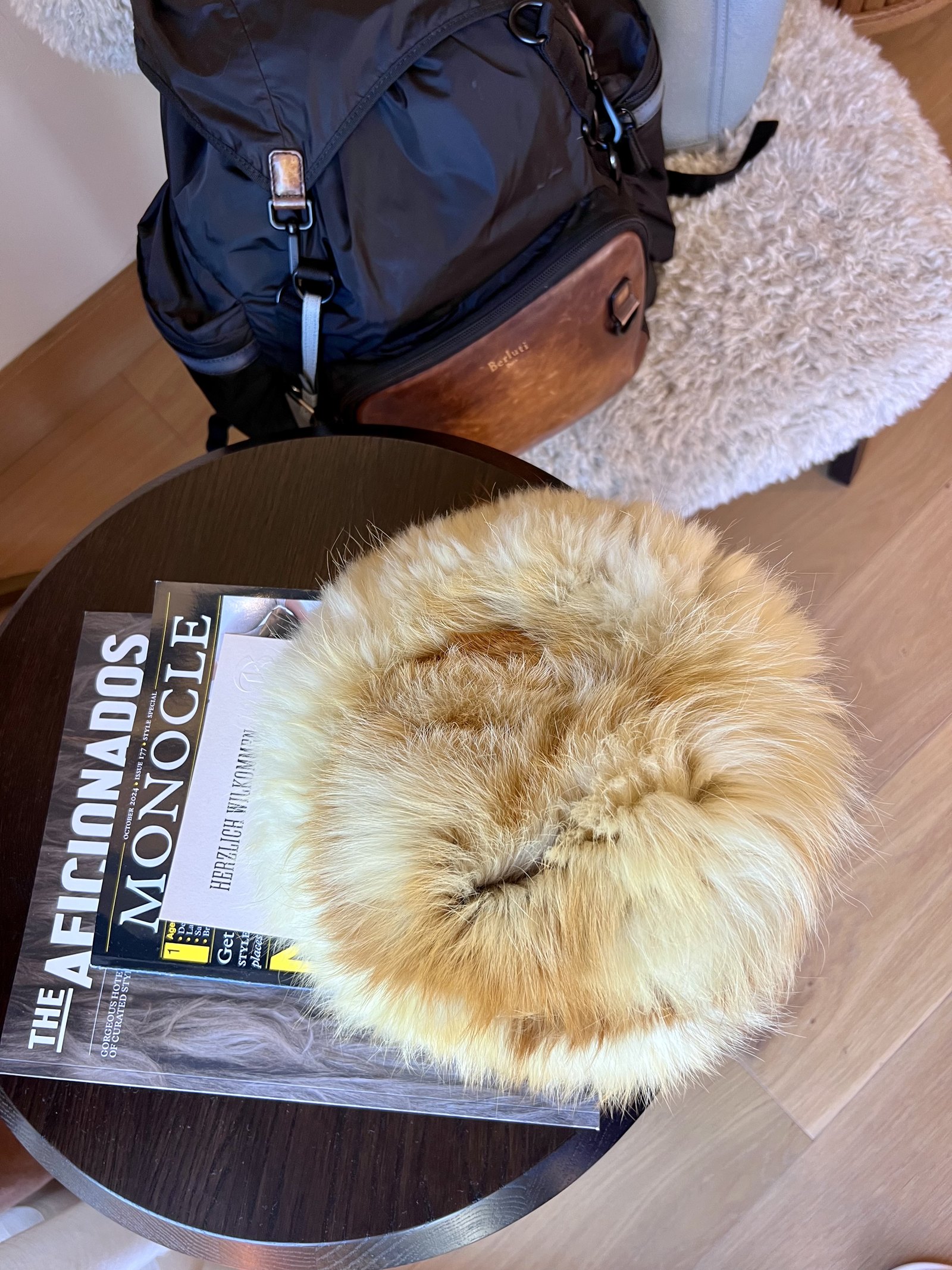 A round sheepskin cushion resting on copies of Monocle and The Aficionados on a dark round table