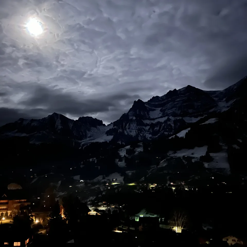 The moon over the dark valley at Adelboden with the lights of the village below