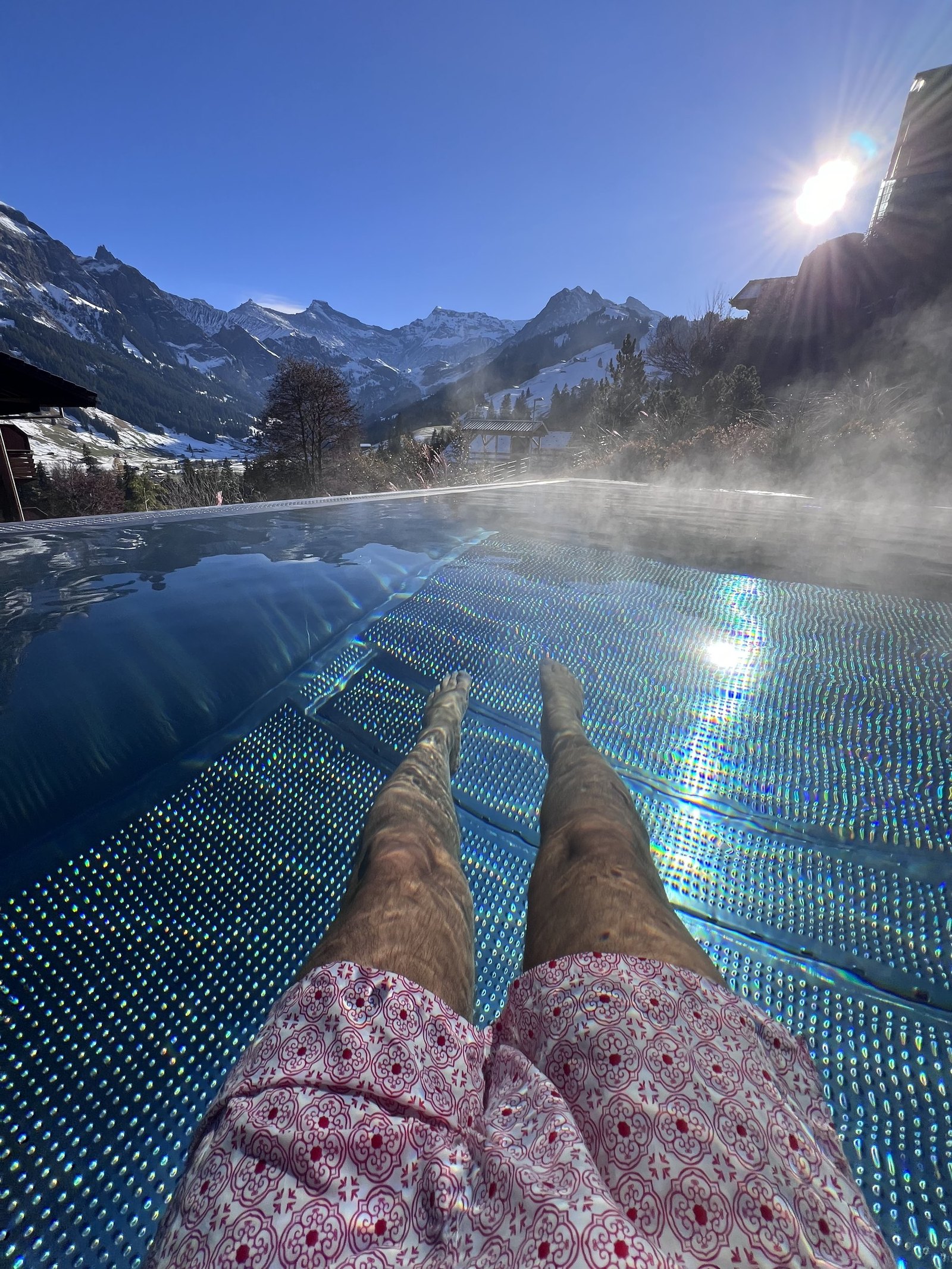 Legs in the heated outdoor pool at The Brecon, steam rising, with the snow on the Adelboden peaks beyond