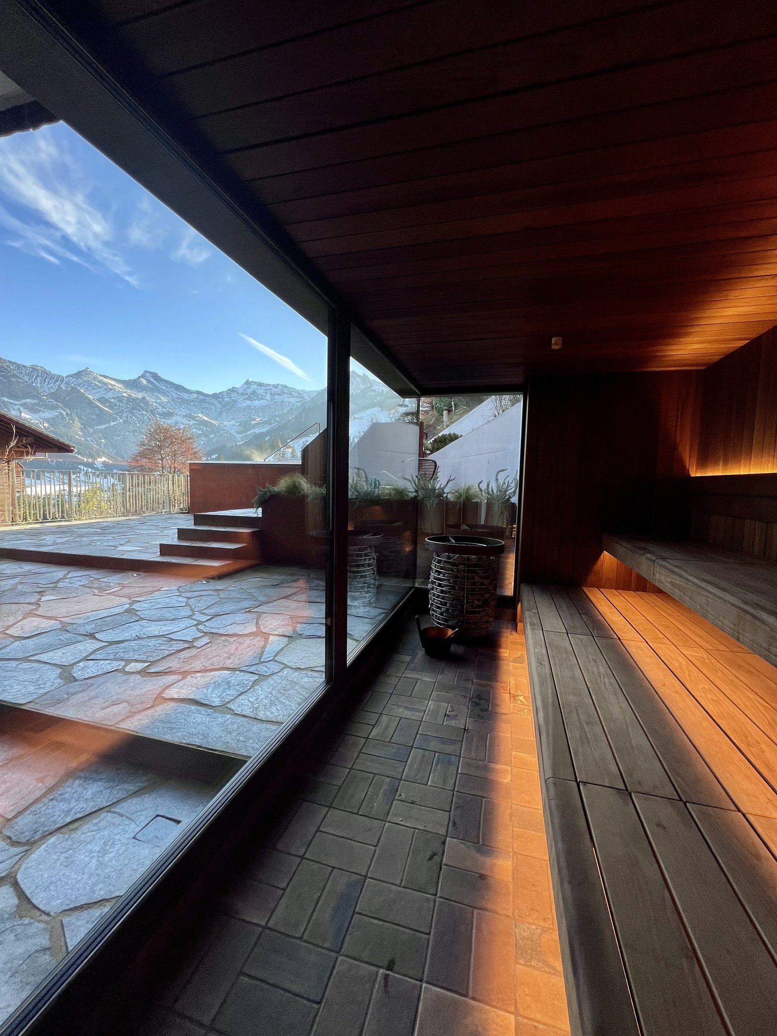 A timber lined spa room with a long low window framing the mountains and a stone floor