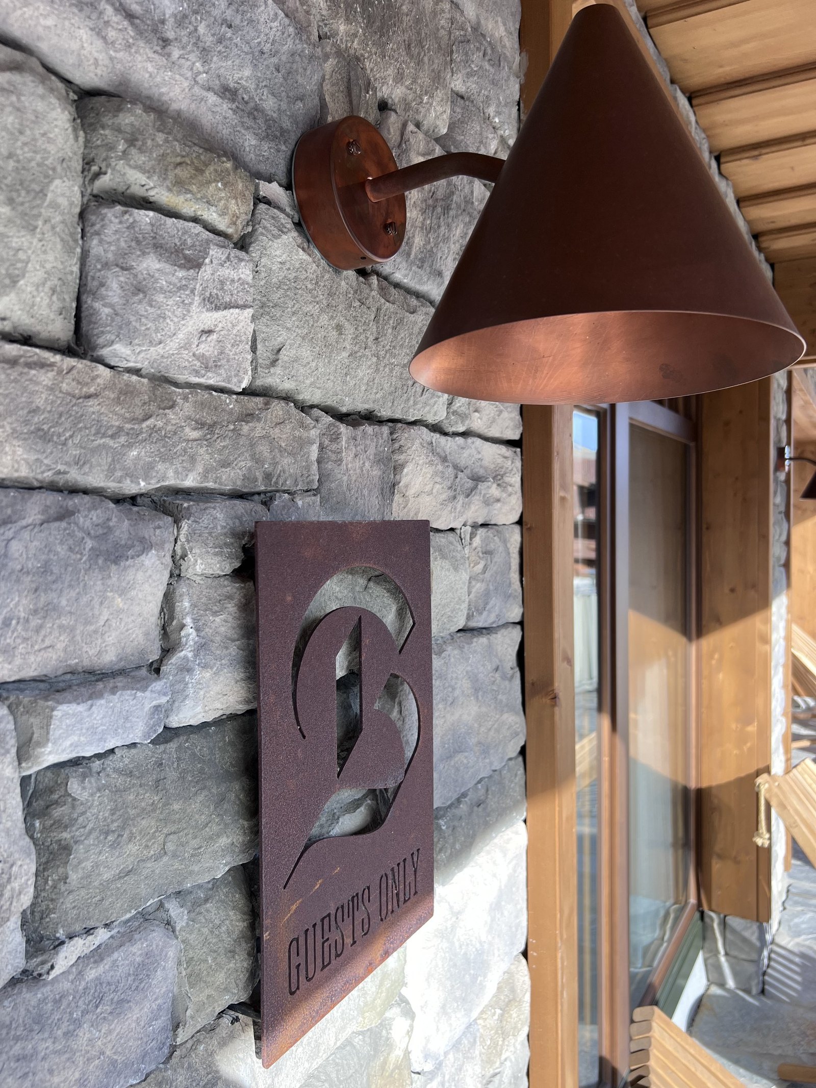 A copper lamp mounted on a stone wall beside a window, with a small plaque below it