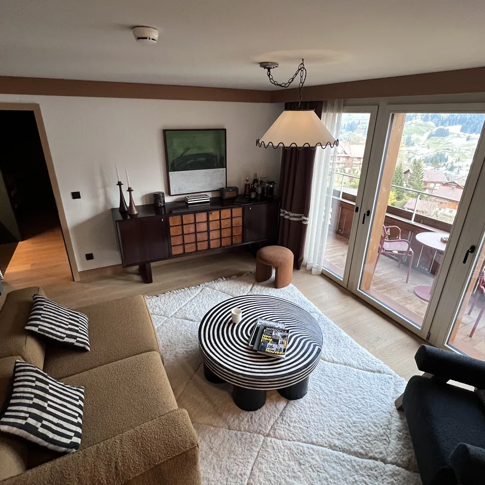 A sitting room at The Brecon with a long sofa, striped cushions and a round striped table, the balcony doors open to the valley