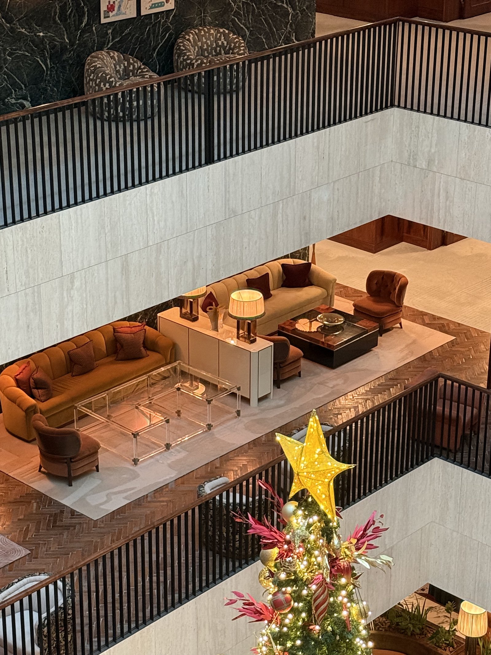 An internal atrium at The Ned Doha seen from an upper balcony, galleries running round it and orange seating on the floor below