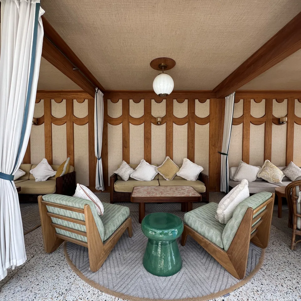 Inside a poolside cabana at The Ned Doha, timber frame, scalloped fabric walls, green and white striped cushions and a green ceramic stool