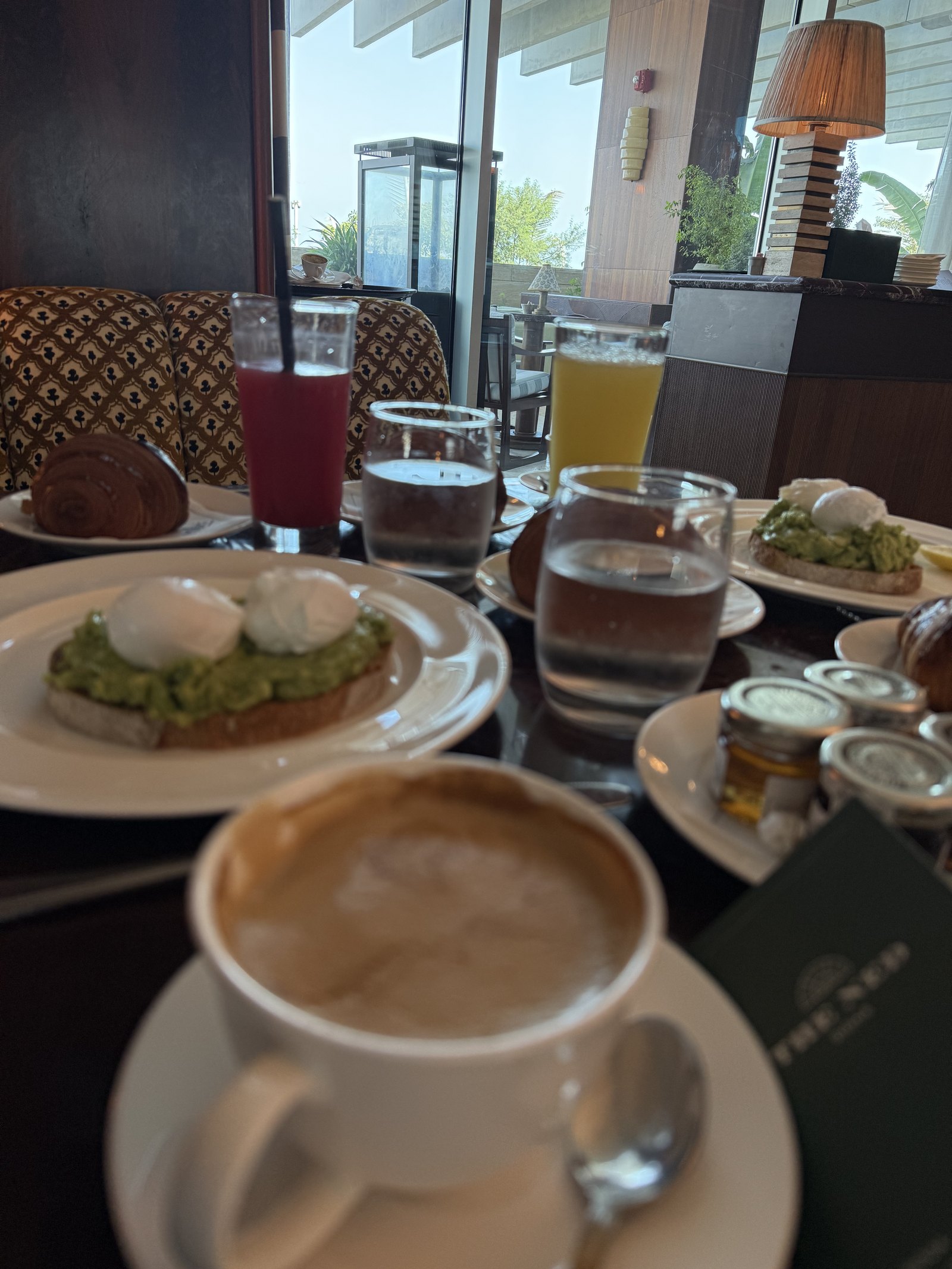 A cup of coffee on a saucer beside a dark green card printed with The Ned, on a breakfast table