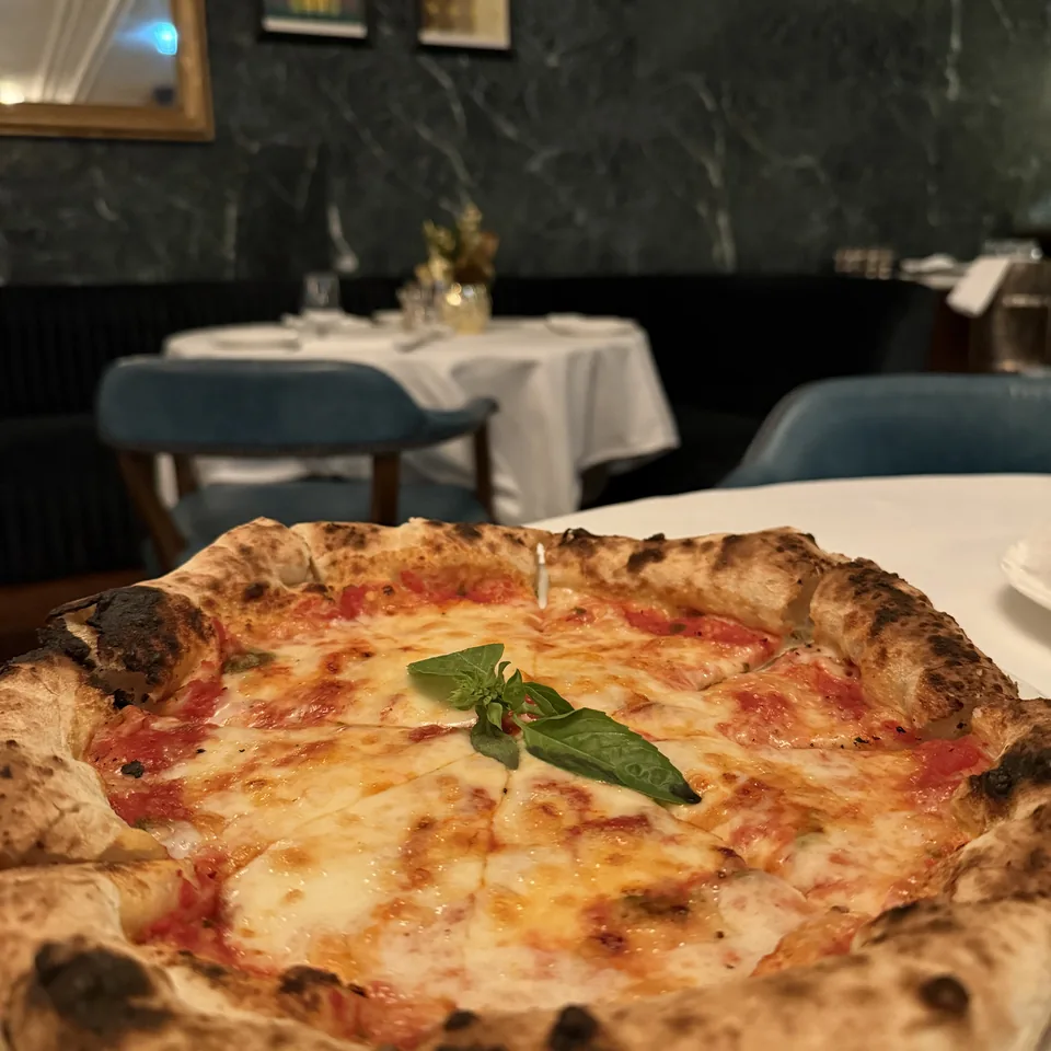 A margherita pizza with a basil leaf on a white plate, the green marble dining room out of focus behind it