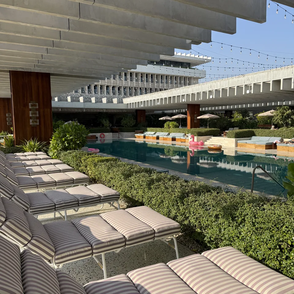 A long row of striped poolside loungers seen end on, with clipped hedges and the concrete colonnade beyond