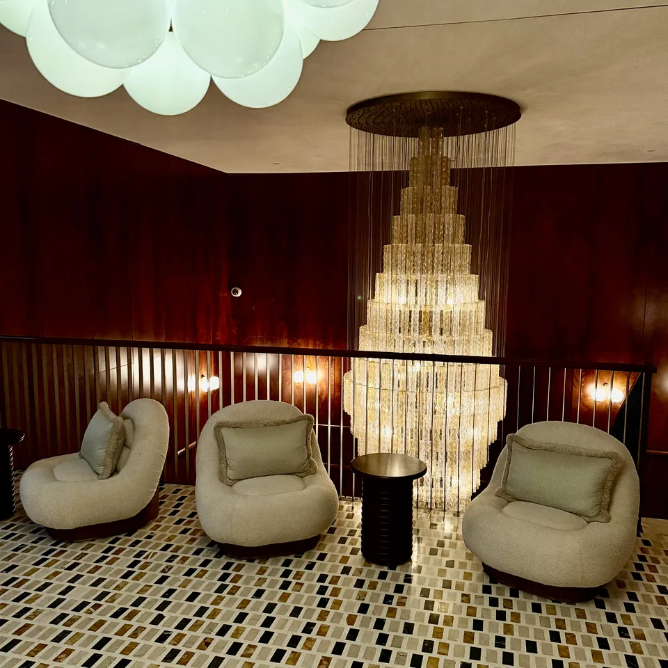 A burgundy panelled room with a tall cascading crystal chandelier over pale curved armchairs and a mosaic floor