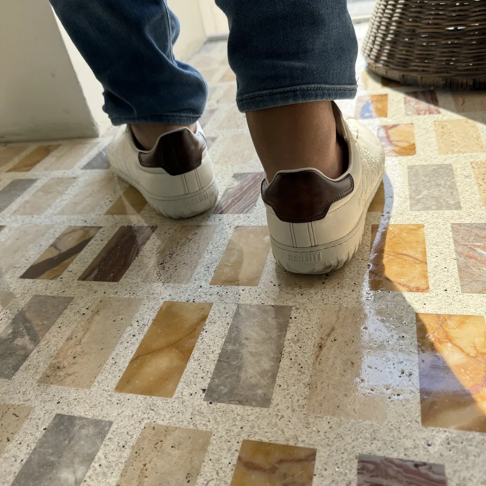 A pair of white trainers from above on a floor of inlaid marble rectangles in cream, ochre and grey