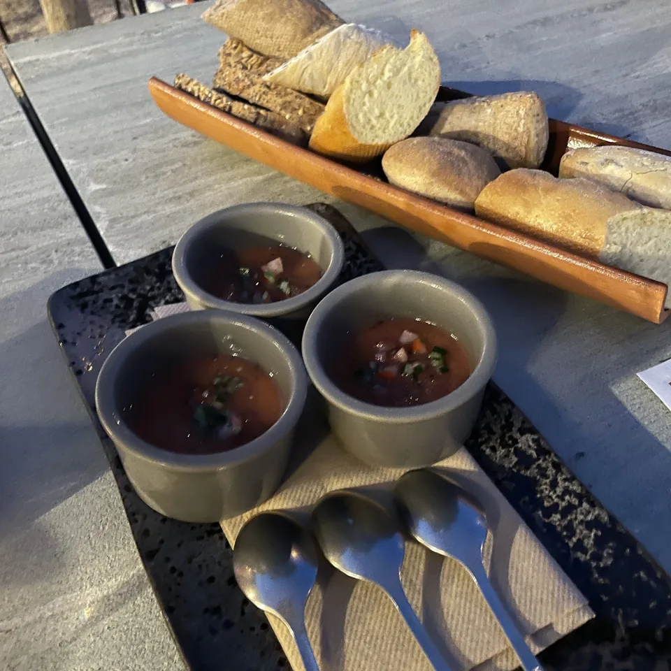 A timber board of breads and three small bowls of dips on a dark stone table at The Rooster, with spoons laid beside them