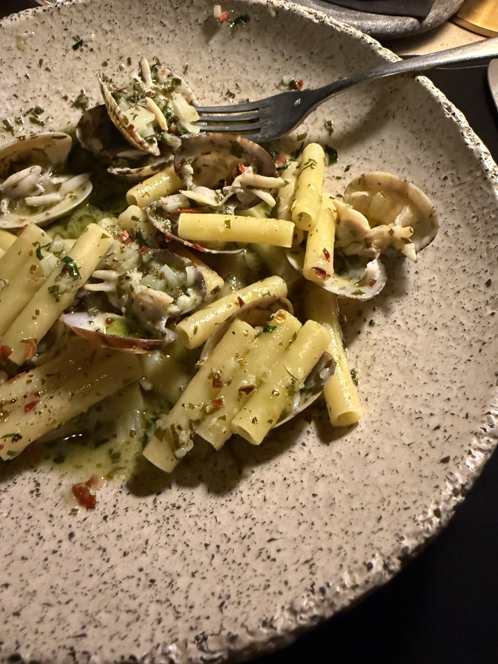 A speckled ceramic bowl of short pasta with clams and chopped herbs at The Rooster, with a fork resting in it