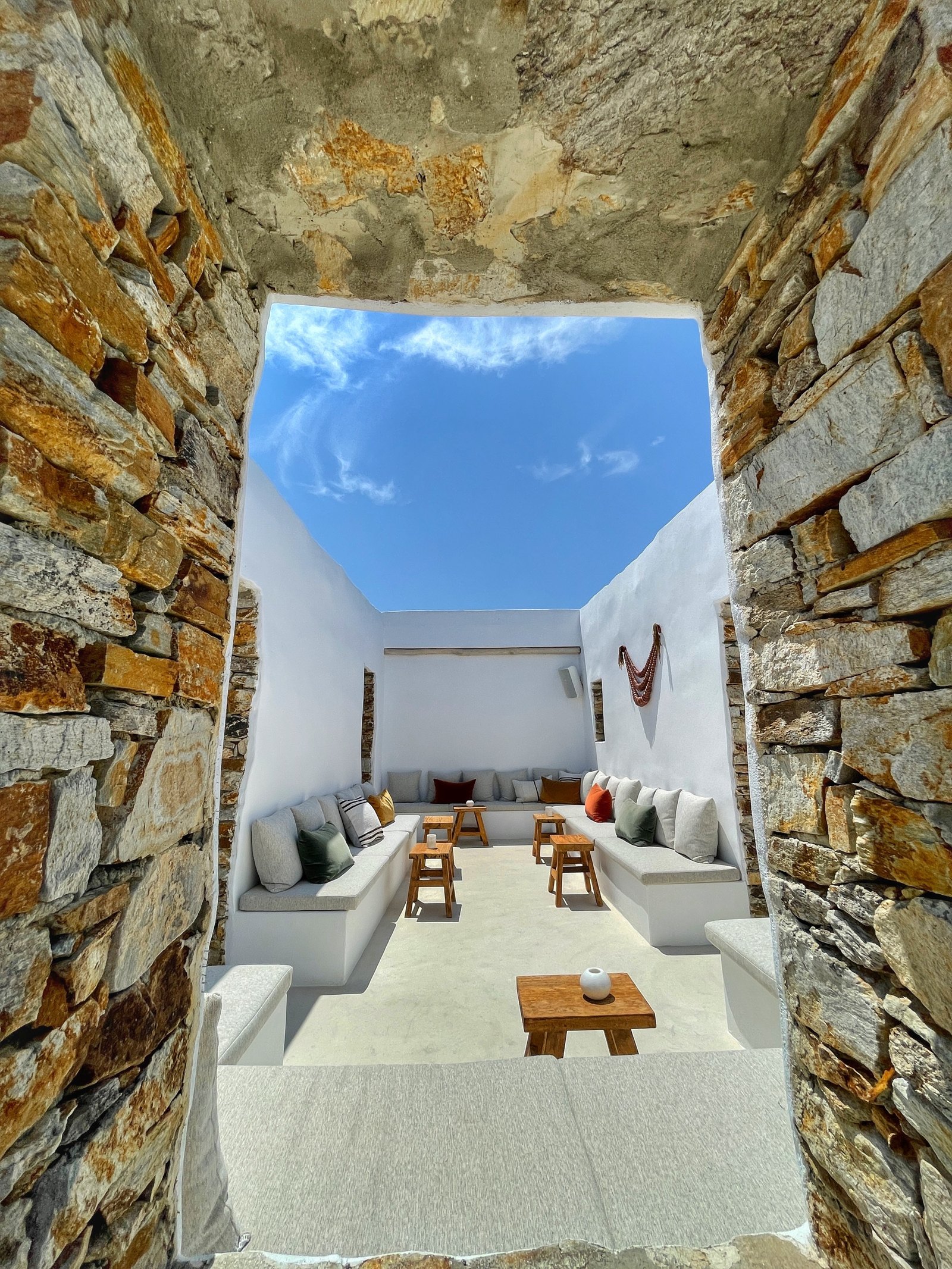 A sunken courtyard at The Rooster walled in rough stone, with built-in seating, white cushions and a hammock strung across the corner under an open square of sky