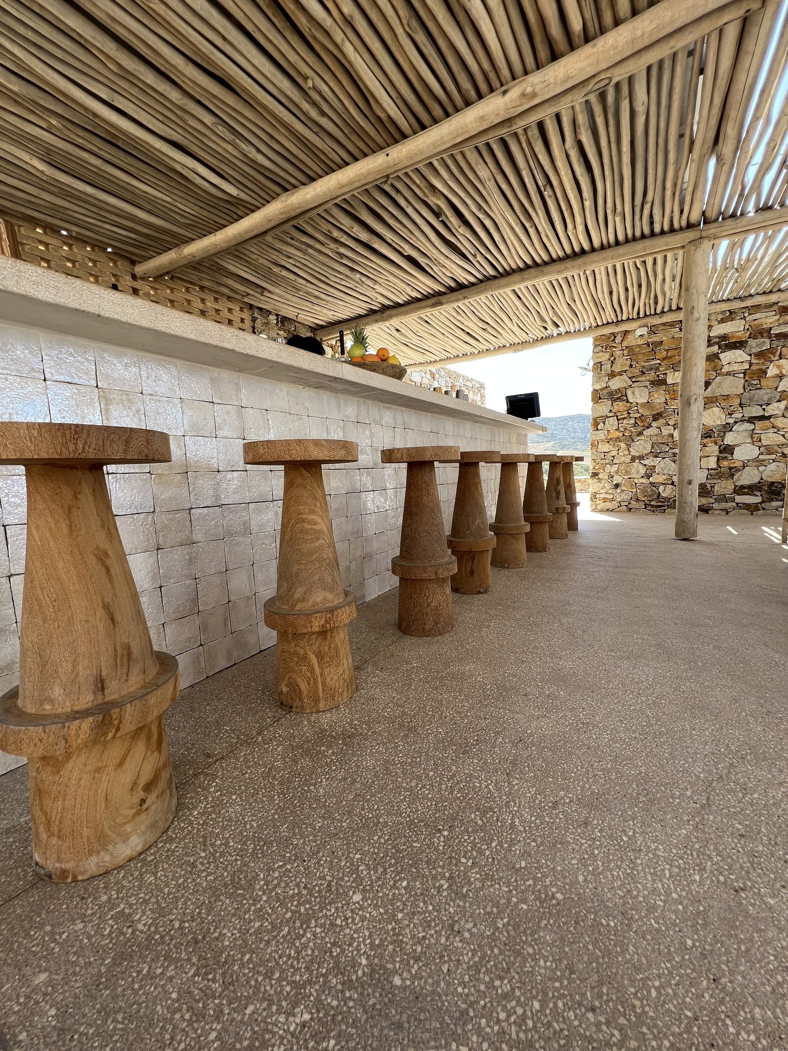 The bar at The Rooster, a counter of pale blocks with heavy turned timber stools along it under a reed ceiling