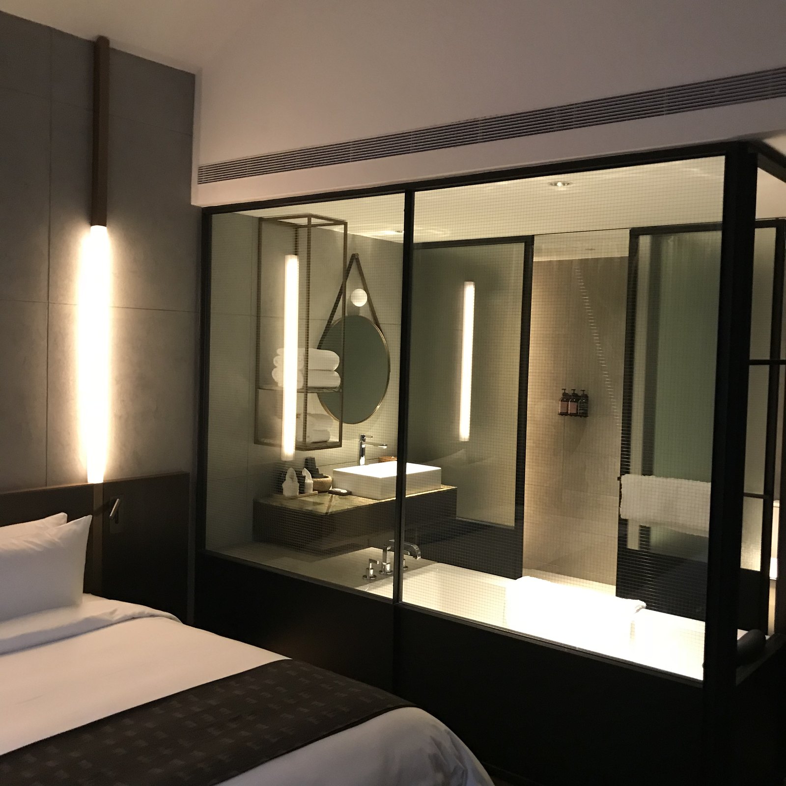 A basin and mirror seen through a black steel and glass partition from the bed