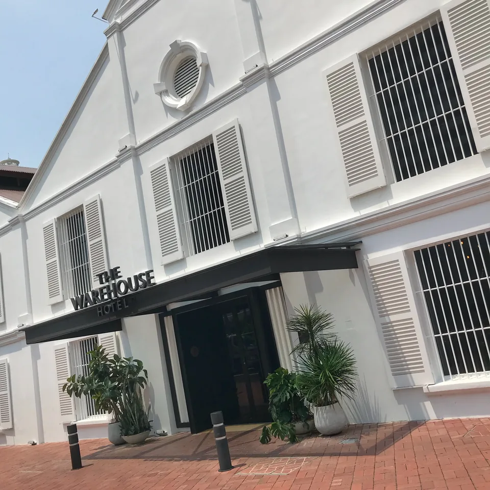 The white godown front at an angle, THE WAREHOUSE HOTEL lettered on the black canopy over the entrance