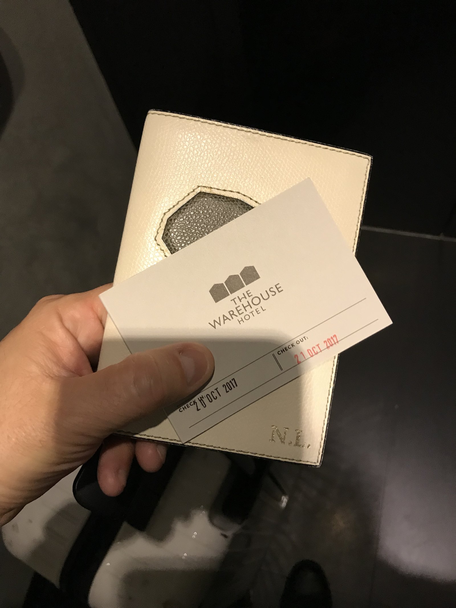 A hand holding a white leather key wallet and a card stamped with the check-in and check-out dates